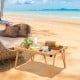 Folding camping table with waterproof surface, set up for a picnic on the beach, featuring a sturdy frame and storage.