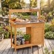 Wooden outdoor garden work station with a large metal tabletop, drawer, and lower shelf for versatile gardening tasks.