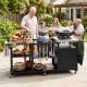 Outdoor grill cart with stainless steel tabletops, hooks, and storage shelves, perfect for family gatherings and BBQs.