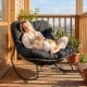 Outdoor Papasan rocking chair with thick black cushion, providing ergonomic support for relaxing on a balcony.