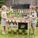 Wooden outdoor mud kitchen for kids featuring stoves, sinks, storage, and blackboards for imaginative play and.