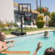 Portable basketball hoop with adjustable height, set by a poolside, featuring a shatterproof backboard and stability.
