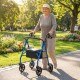 Senior woman using a blue rollator walker with seat, featuring adjustable handles, in a sunny park setting.
