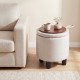 Beige round storage ottoman with removable lid, upholstered in soft linen fabric, serving as a footrest and side table.