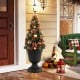 Vintage black planter with pedestal base, showcasing a decorative Christmas tree for outdoor porch decoration.