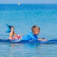 Child lying on a 6-foot foam surfboard in the ocean, perfect for beginners with a durable foam top and removable fins.