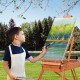 Young artist using a Tripod Folding French Wooden Easel with Sketch Box outdoors, perfect for painting and drawing.