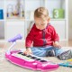 Child playing with a pink 37-key electronic keyboard toy piano, featuring a detachable microphone and sturdy design.