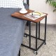 Mobile side table with a brown wood top and black metal frame, ideal for use beside a bed or sofa.