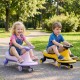 Two children riding the Wiggle Car Ride-on Toy in yellow and purple, featuring flashing wheels for outdoor fun.